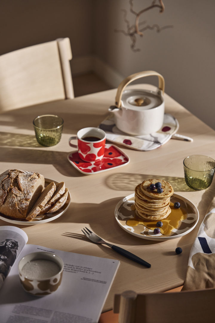 Et frokostbord dekket med Marimekko Unikko tallerkener og tekanne og en stabel pannekaker med sirup.