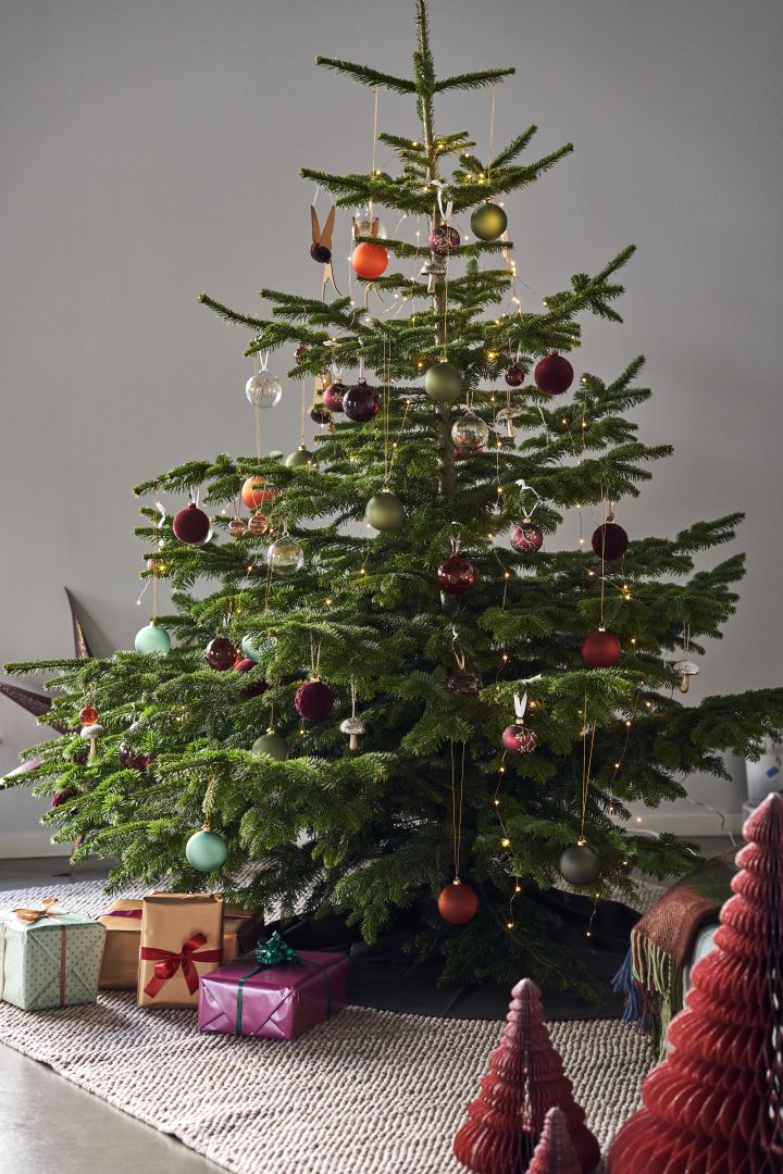 Pynt juletreet med juletrepynt i 4 forskjellige stiler i henhold til Nest Trends - Nurture, Share, Boost and Cultivate. Her ser du et praktfullt tre på Scandi Living Flock ullteppe i beige med dekorasjoner i dype fyldige farger og nyanser av rødt, oransje og grønt.